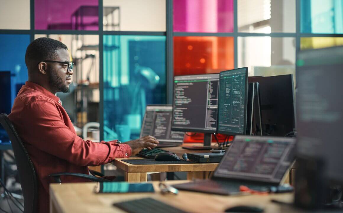 Man seated in front of multiple screens with colourful background