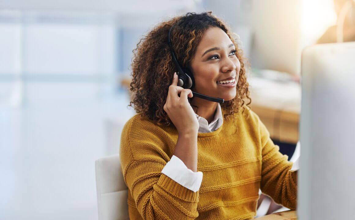 Customer Service Representative wearing a yellow sweater while smiling and talking to a customer