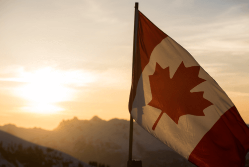 the Canadian flag is backlit by a sunset