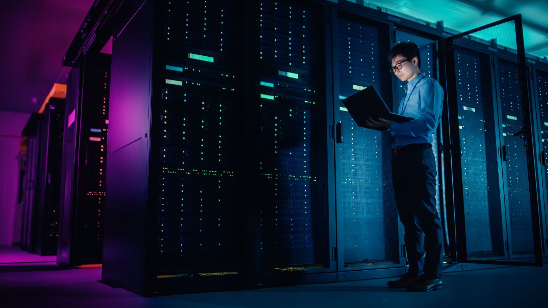 A man standing holding a laptop while in a data center.